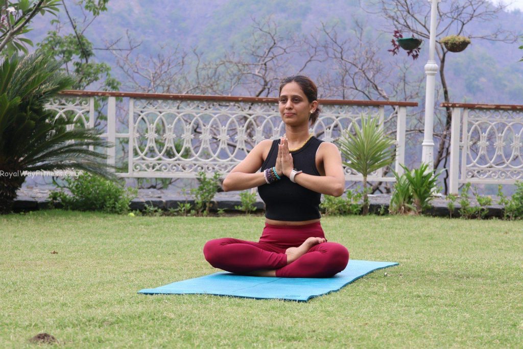 Woman meditating on a yoga mat outdoors.